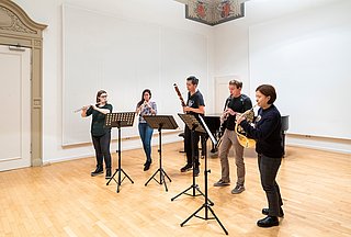 Bläserkammermusikensembles stehen vor Notenpulten und spielen auf ihren Instrumenten 